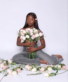 a woman sitting on the ground with flowers around her