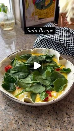 a white plate topped with spinach and cheese on top of a counter next to a glass