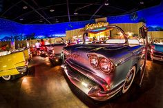 several classic cars are on display in a showroom at an automobile museum, with brightly colored lights shining from the hoods