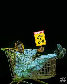 a man sitting in a shopping cart holding a sign that says opera opi ta on