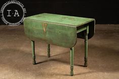 an old green wooden desk sitting on top of a cement floor next to a black wall