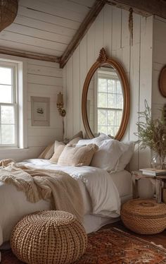 a bedroom with white bedding and pillows, round mirror on the wall above it