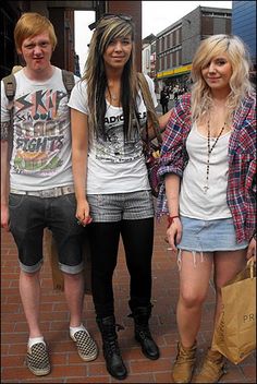 three young people standing next to each other on a brick walkway in front of buildings