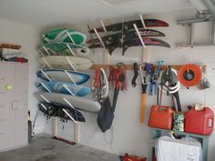 there are many surfboards hanging on the wall in this garage with hooks and other items