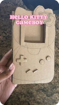 a hand holding up a cardboard box with an image of a hello kitty gameboy on it