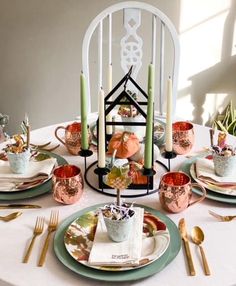 a table set with plates, cups and candles