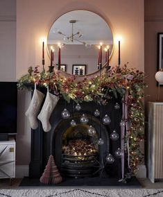 a decorated fireplace with stockings and christmas decorations in front of a round mirror on the wall