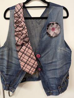 a denim vest with pink and white flowers on it hanging from a black hanger