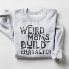 a sweatshirt with the words weird moms build character printed on it, sitting on a white surface