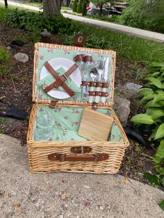 a wicker picnic basket with utensils and plates in it sitting on the ground