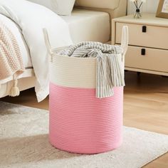 a pink and white basket sitting on top of a wooden floor next to a bed