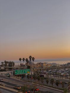 the sun is setting over an intersection with palm trees in the foreground and cars on the road