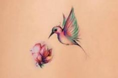 a hummingbird flying next to a flower on the back of a woman's stomach