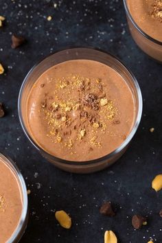 three glasses filled with chocolate pudding on top of a black table next to some nuts