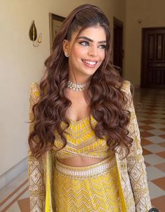 a woman with long brown hair wearing a yellow outfit and smiling at the camera while standing in a hallway