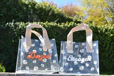 two clear bags sitting on top of a stone wall next to each other with orange and white lettering