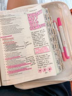 an open bible with pink writing on it and some pens in the bottom half of the book