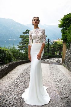 a woman in a white dress is standing on a cobblestone road and posing for the camera