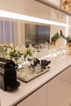 the counter is full of glasses and vases with flowers in them, along with an espresso machine