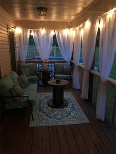 an outdoor living room with white curtains and lights on the ceiling, along with green couches