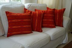 four red and orange pillows sitting on top of a white couch next to a window