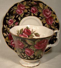 a tea cup and saucer decorated with pink roses on black, gold trimmings