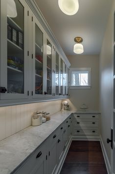 an empty kitchen with white cabinets and wood flooring on the walls, along with recessed lighting