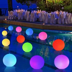 colorful balls are floating on the water in front of an outdoor pool at night time