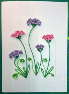 some paper flowers on a white card with green stems and purple petals in the middle