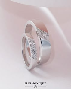 two white gold wedding rings with diamonds on top and bottom, against a light pink background