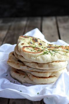 a stack of pita bread sitting on top of a white napkin next to a wooden table