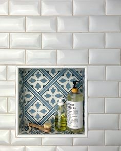 a white tile wall with blue and white tiles in the corner next to a wooden brush