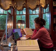 a woman sitting at a desk in front of a laptop computer with books on it