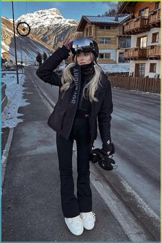 a woman standing on the side of a road with skis in her hand and snowboarding gear around her neck