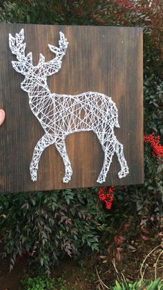 someone holding up a string art deer on a wooden sign with red berries in the background