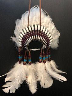 "\"WHITE WIND\" Mini Head Dress with back feathers - Hand Made in the USA! Measures approximately 6 inches across and dangles a least 12 inches and the depth is at least 8 inches with the feathers. Made in the USA by Jasmine Battle, Cherokee Artist Burgundy and White spaghetti beads White Bottom Turkey Feathers and White Back Feathers Burgundy, Dark Chocolate & Turquoise Beads If you have a customization REQUEST you would like, send that in a message please. A Certificate of Authenticity is Safety Pin Crafts, Head Dresses, Car Charms Rear View Mirror, Safety Pin Jewelry, Native Dress, White Spaghetti, Indian Headdress, Paint Horse, Beadwork Designs