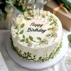 a birthday cake with white frosting and flowers on it, surrounded by greenery