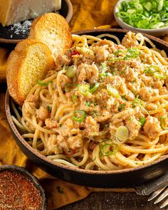 a bowl filled with pasta and meat on top of a table next to bread slices