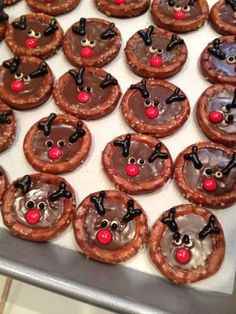 chocolate covered pretzels decorated with reindeer noses and antlers are on a baking sheet