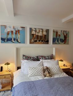 a bed with two pictures on the wall above it and a teddy bear sitting on top