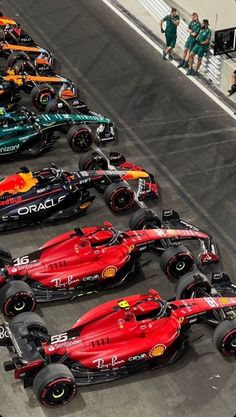 several red and green race cars lined up in a row on the track with people watching