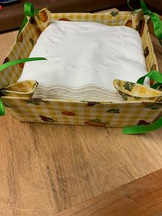 an empty paper box sitting on top of a wooden table with green ribbon around it