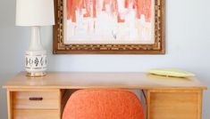 an orange chair sits in front of a desk with a painting on the wall behind it