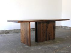 a wooden table sitting on top of a cement floor next to a white wall in an empty room