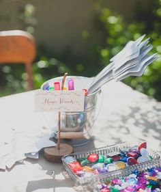 a table topped with lots of candy next to a metal bowl filled with lollipops