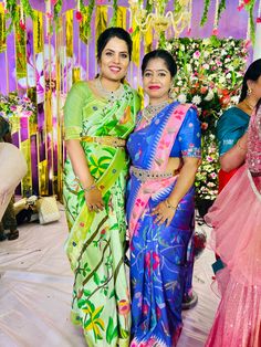 two women standing next to each other in colorful sari dresses and smiling at the camera