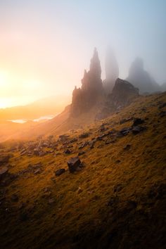 the sun is setting over some rocks on a grassy hill with fog in the air