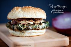 a turkey burger with spinach and goat cheese on a cutting board next to an onion wedge