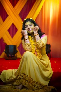 a woman sitting on the ground with her hands up to her face and wearing yellow clothing