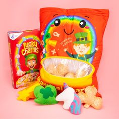 lucky charms are sitting next to an orange pillow and some other toys on a pink background